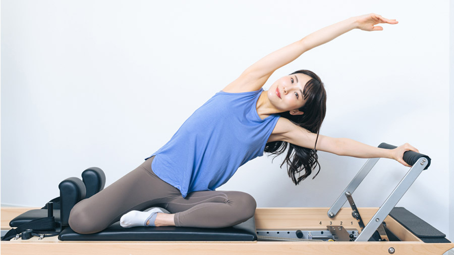 ピラティスマシンの上で、サイドストレッチを行う女性。